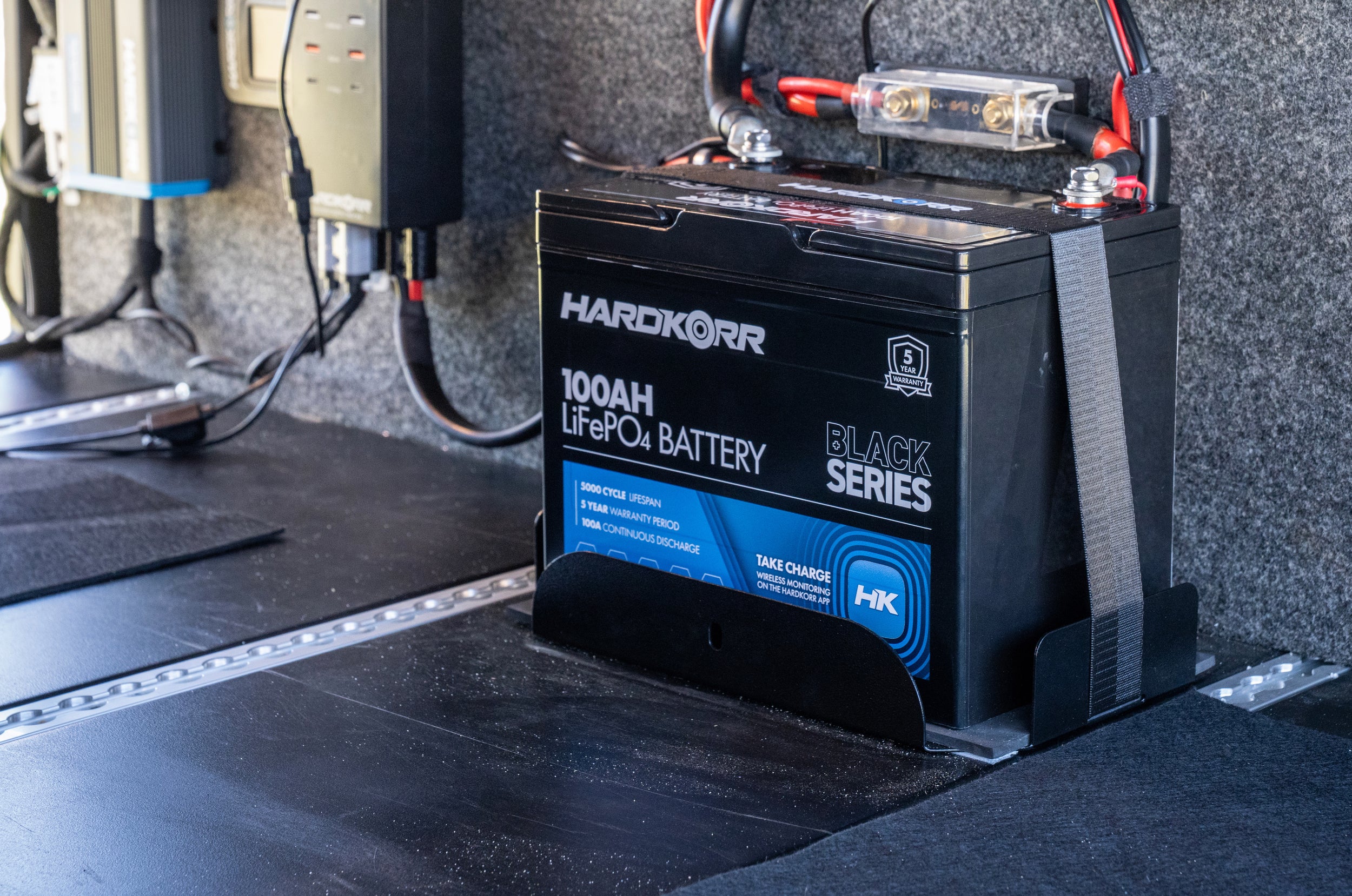 Hardkor 100Ah LiFePO4 battery on a vehicle interior with wiring.